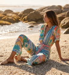 Woman in a cream or light beige elegant jumpsuit, seated in a relaxed pose, showing the flowing fabric and chic summer style.