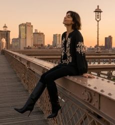 Black long-sleeve peasant blouse, v-neck tie, cream floral embroidery, linen-look, model seated at sunset.