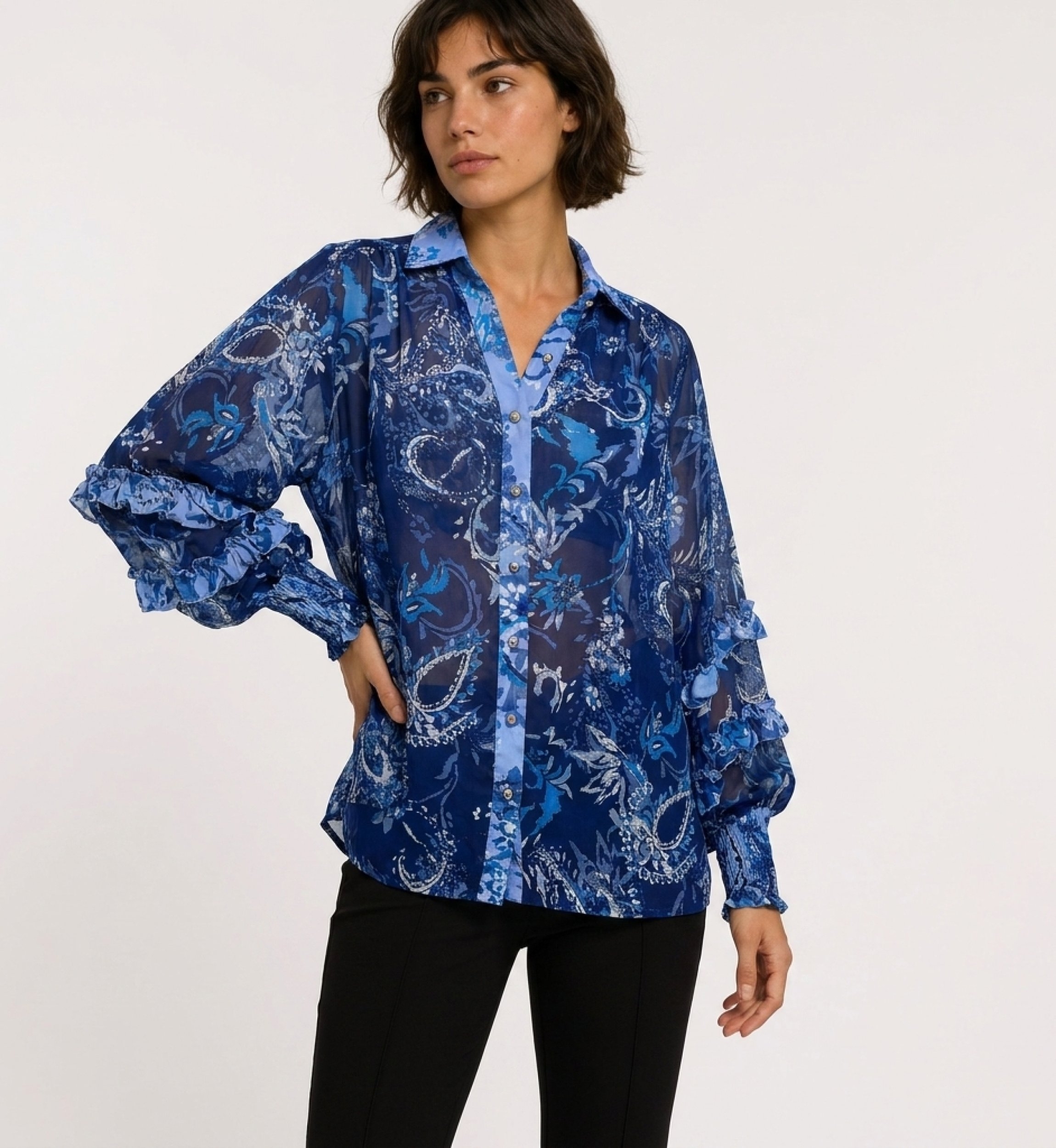Vista tres cuartos de blusa azul transparente de manga larga con estampado floral cachemir, puños con volantes y cuello V.