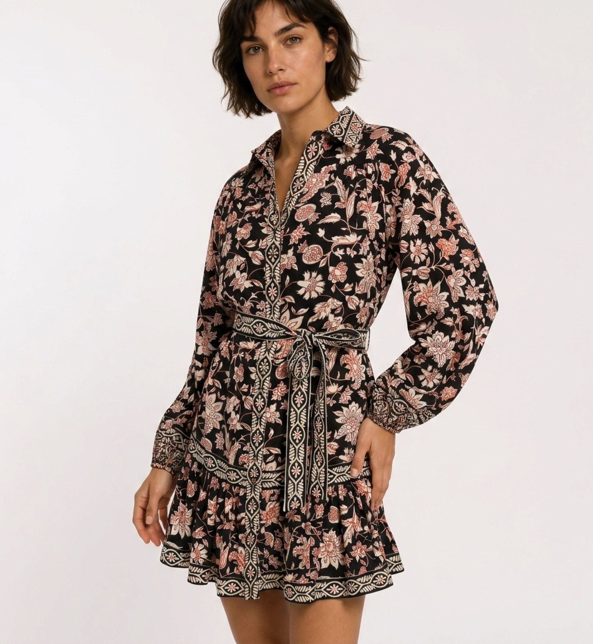 Vestido mini negro de manga larga con estampado floral rojo y crema, cuello, cinturón anudado y falda de volantes escalonados.