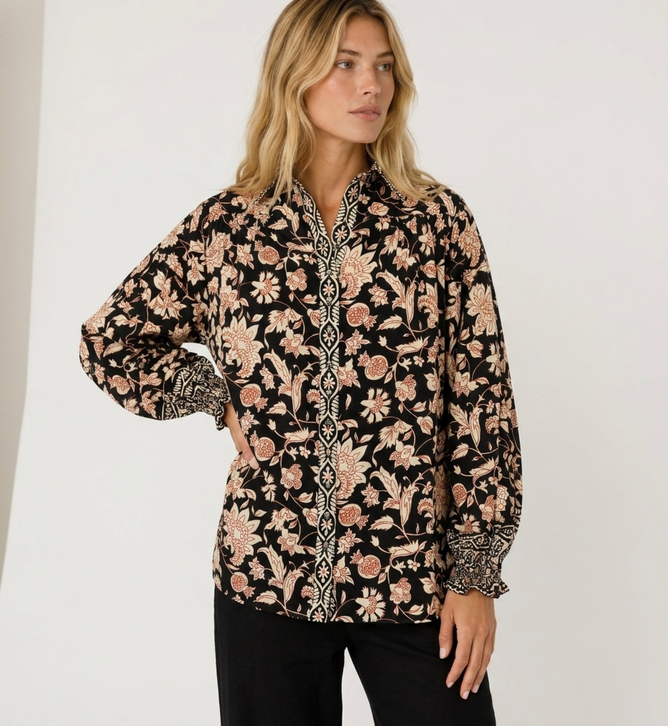 Blusa preta de manga comprida com estampa floral creme e ferrugem, gola e punhos com babados em tecido leve.