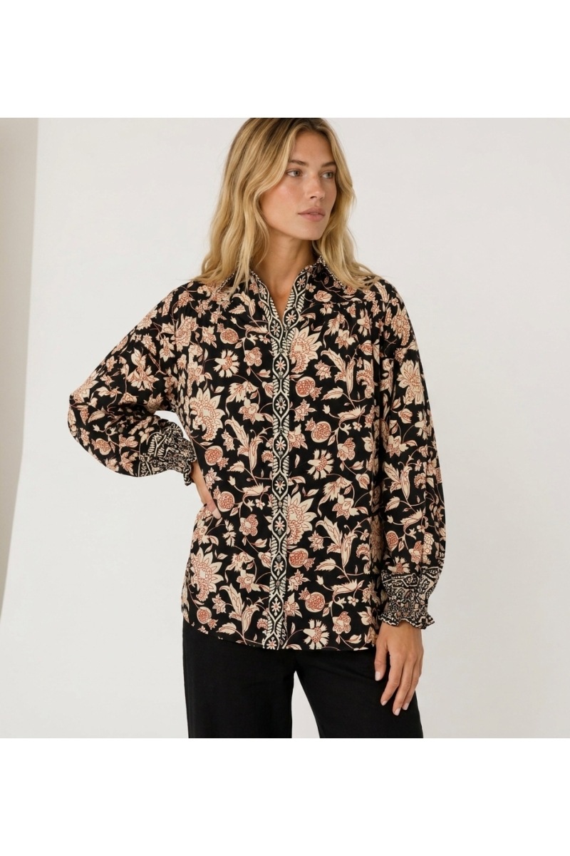 Blusa negra de manga larga con estampado floral crema y óxido, cuello y puños con volantes de tela ligera.