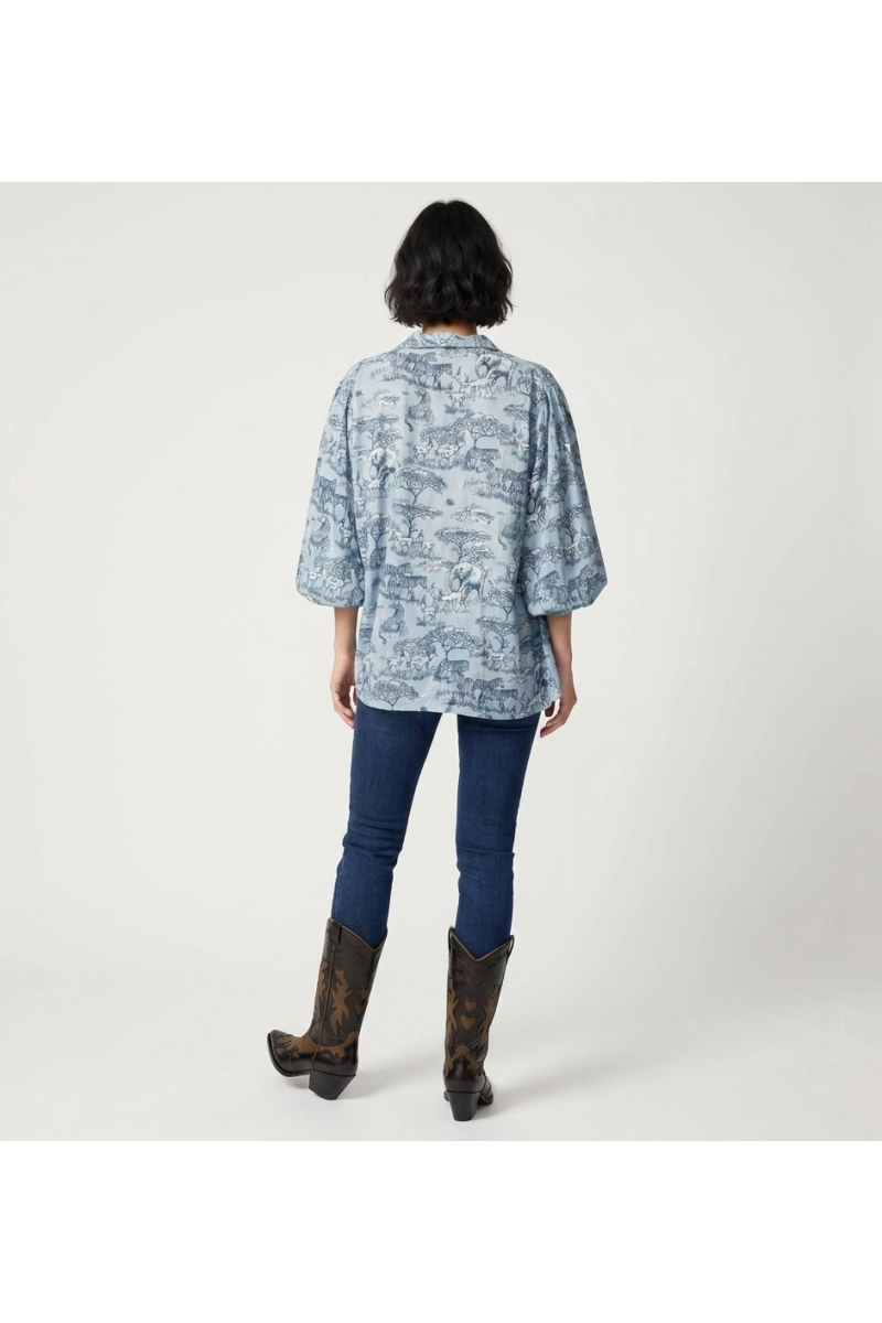 Camisa abotoada azul claro de manga comprida, vista traseira. Estampa de animais safari azul/branco, mangas bufantes franzidas.