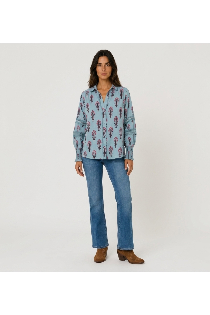 Camisa azul clara floral com botões, decote em V, mangas bufantes com renda e punhos franzidos. Vista frontal.