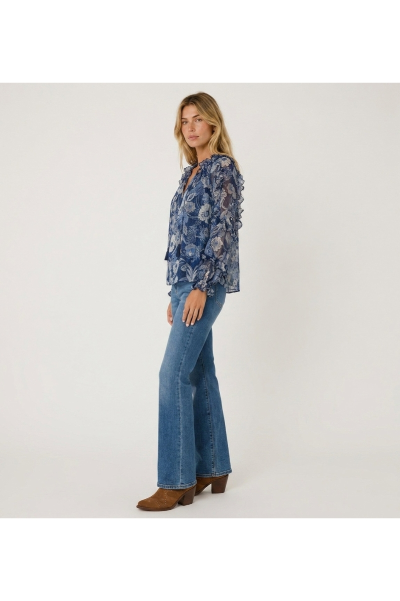 Three-quarter view of a sheer blue floral long-sleeve blouse with ruffled shoulders, cuffs, and drawstring neckline.