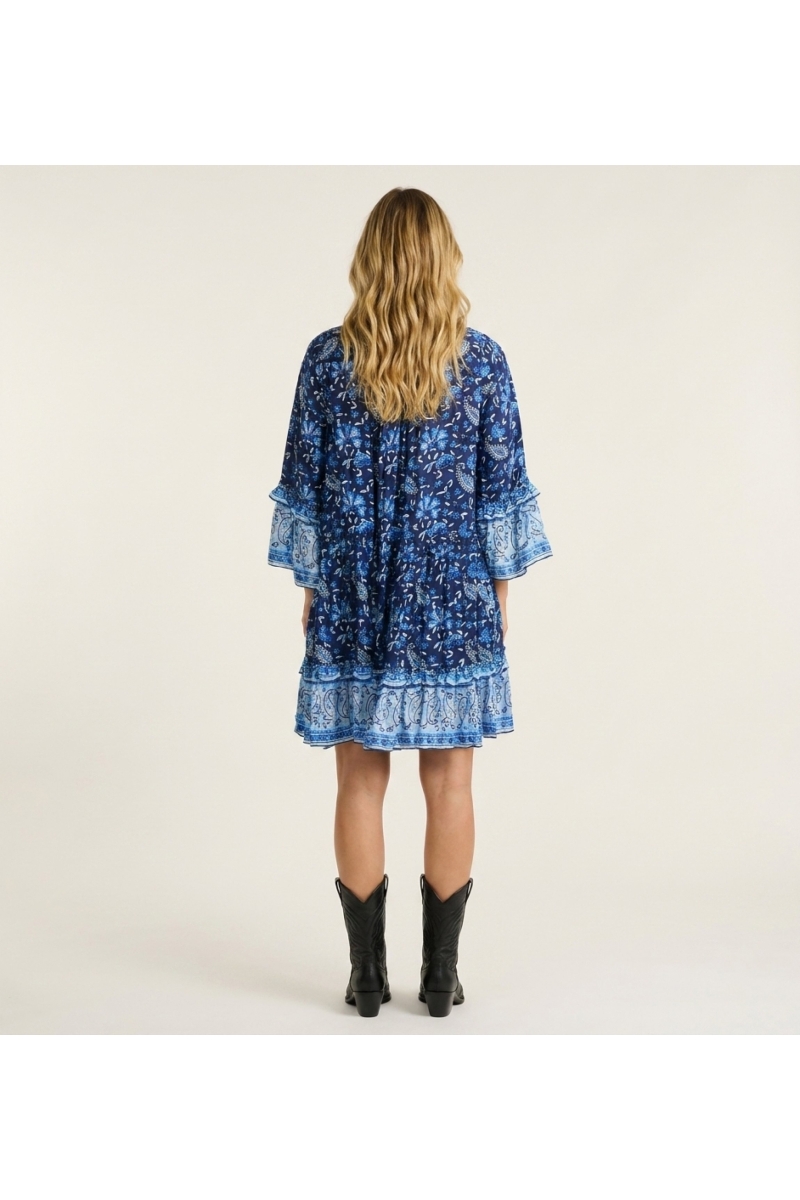 Costas de mini vestido azul e branco com padrão paisley floral, decote V com gola, mangas três quartos com folhos e saia em cama