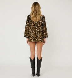 Back view of a loose black blouse with gold white leopard print, ruffled neckline, and black pom-pom tassel trim.