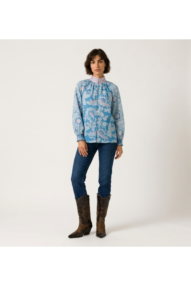 Vista frontal de blusa azul de manga comprida com estampa floral rosa e branca, gola alta e caimento solto.