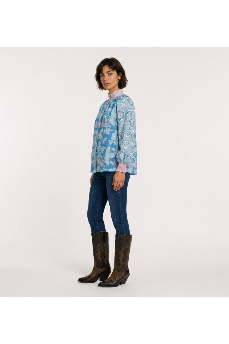 Blue long-sleeve floral blouse with pink and white flowers, high neck, loose fit, cotton-like fabric, three-quarter view.