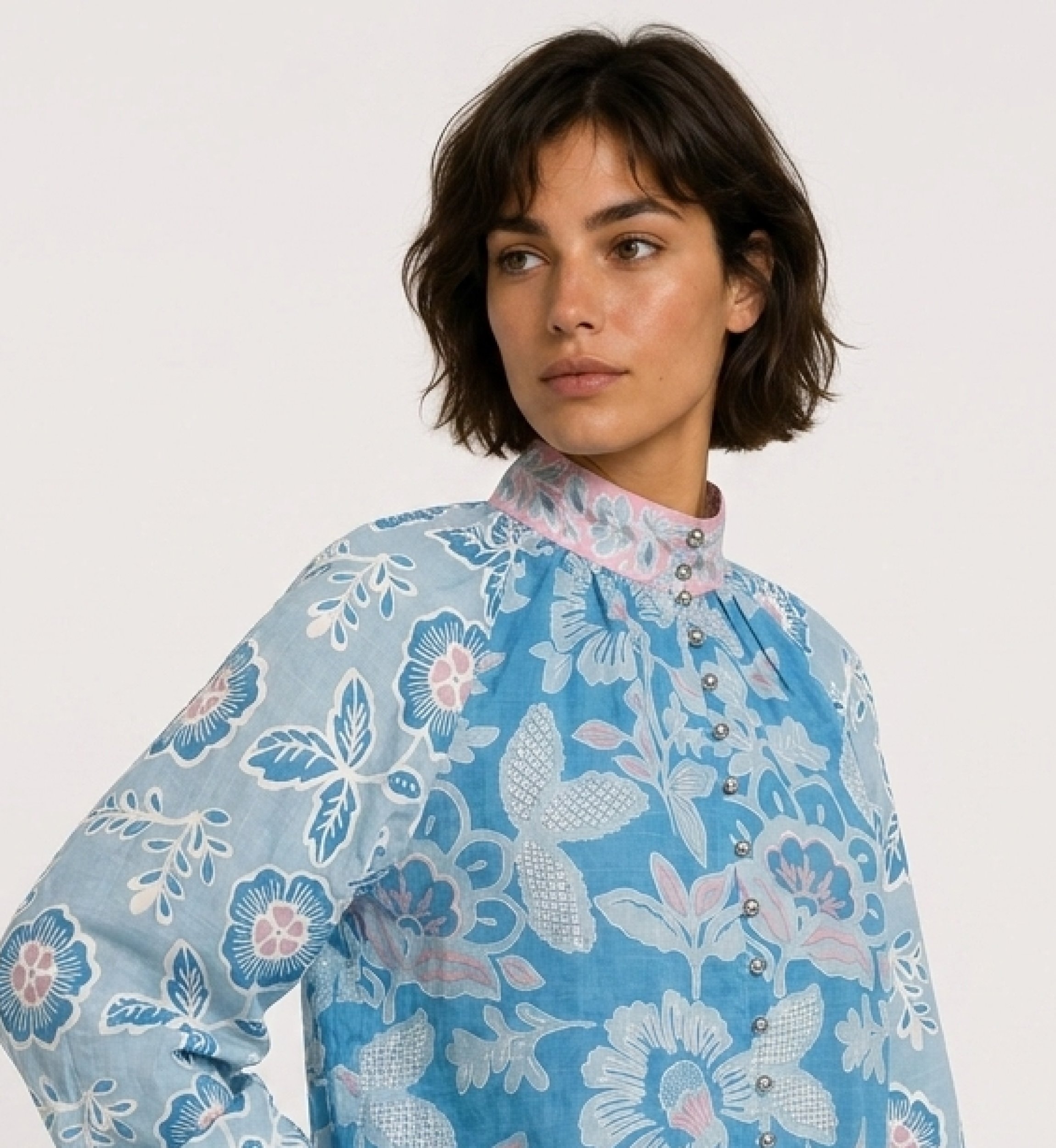 Three-quarter side view of a blue long-sleeve floral blouse with pink and white patterns, high neck, and loose fit in soft cotto
