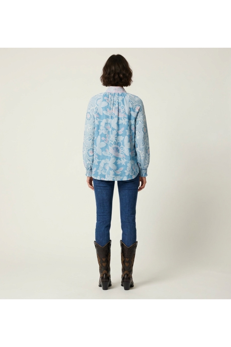 Blusa de mujer azul con estampado floral rosa y blanco, manga larga, cuello alto, corte holgado, vista trasera.