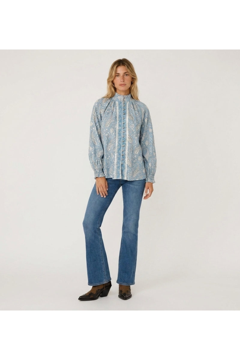 Blusa azul claro de manga longa com estampa paisley branca, gola alta, abotoada na frente e punhos com babados.