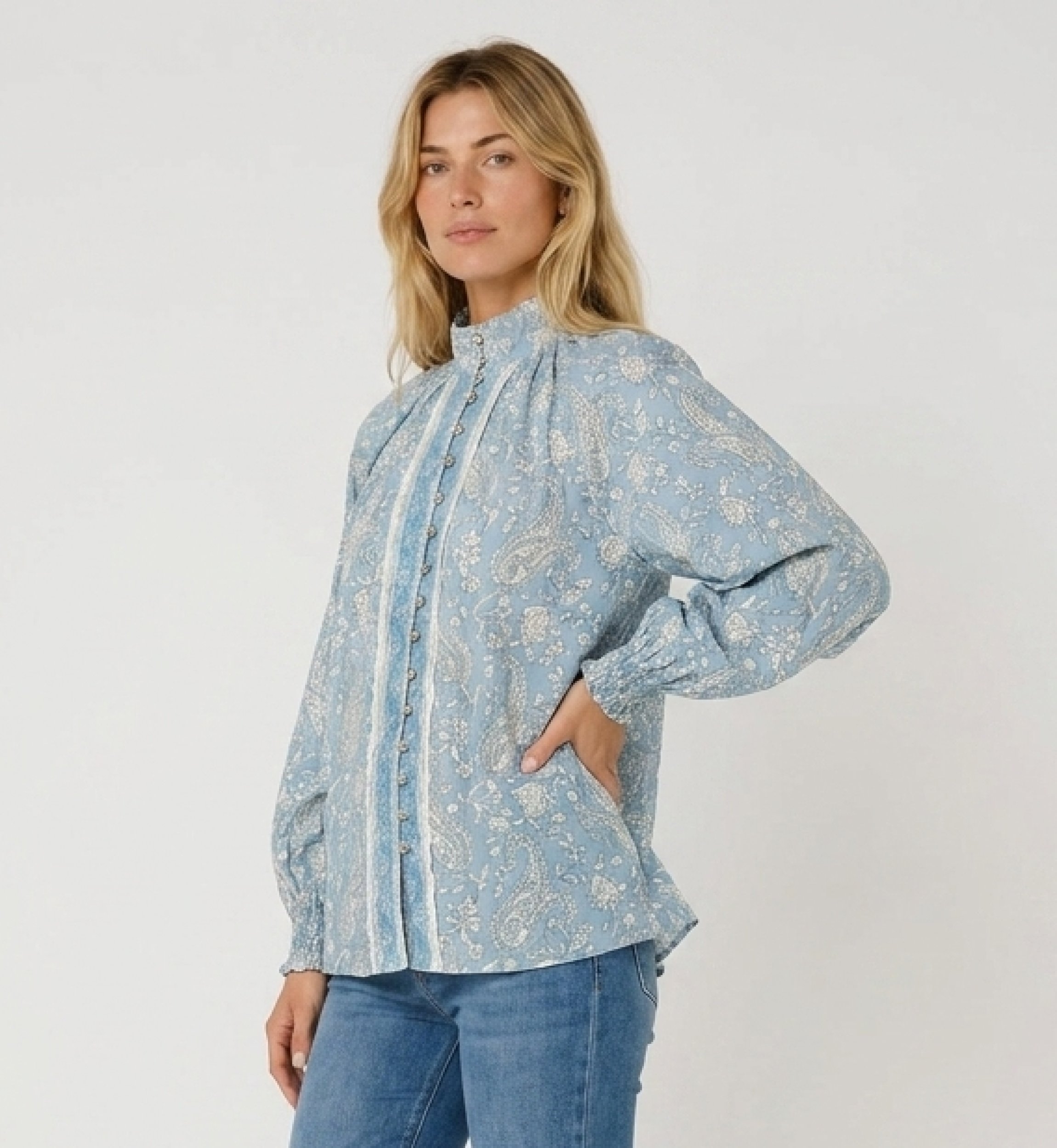 Light blue long-sleeve blouse with white paisley pattern, high collar, button-down front, and ruffled cuffs, three-quarter view.