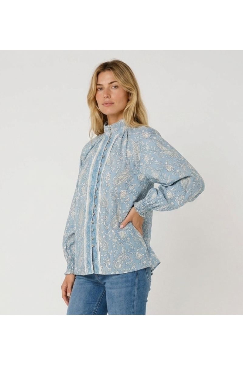 Light blue long-sleeve blouse with white paisley pattern, high collar, button-down front, and ruffled cuffs, three-quarter view.