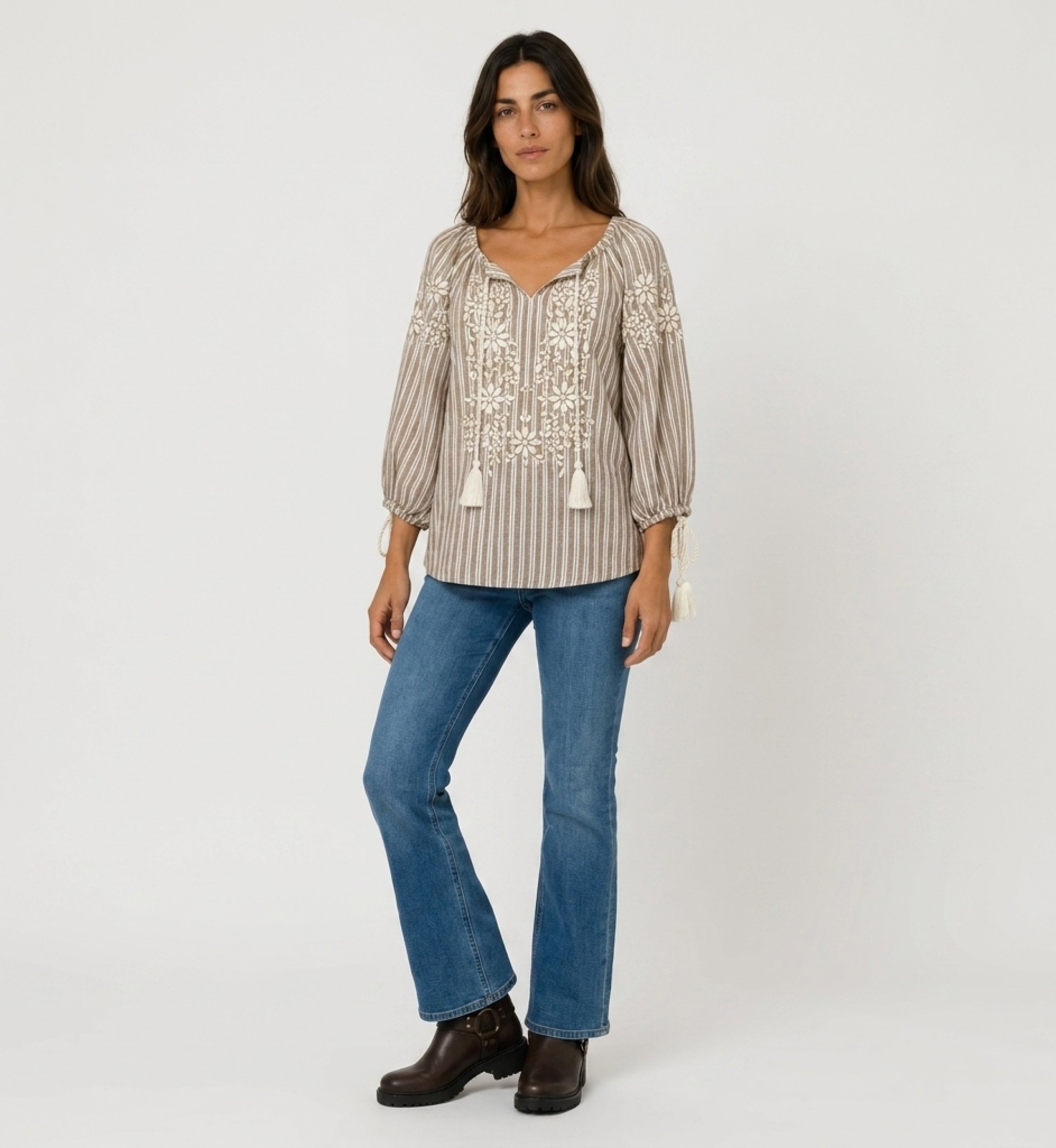 Front view of a brown and white striped peasant blouse with v-neck, 3/4 balloon sleeves, white floral embroidery, and tassels.