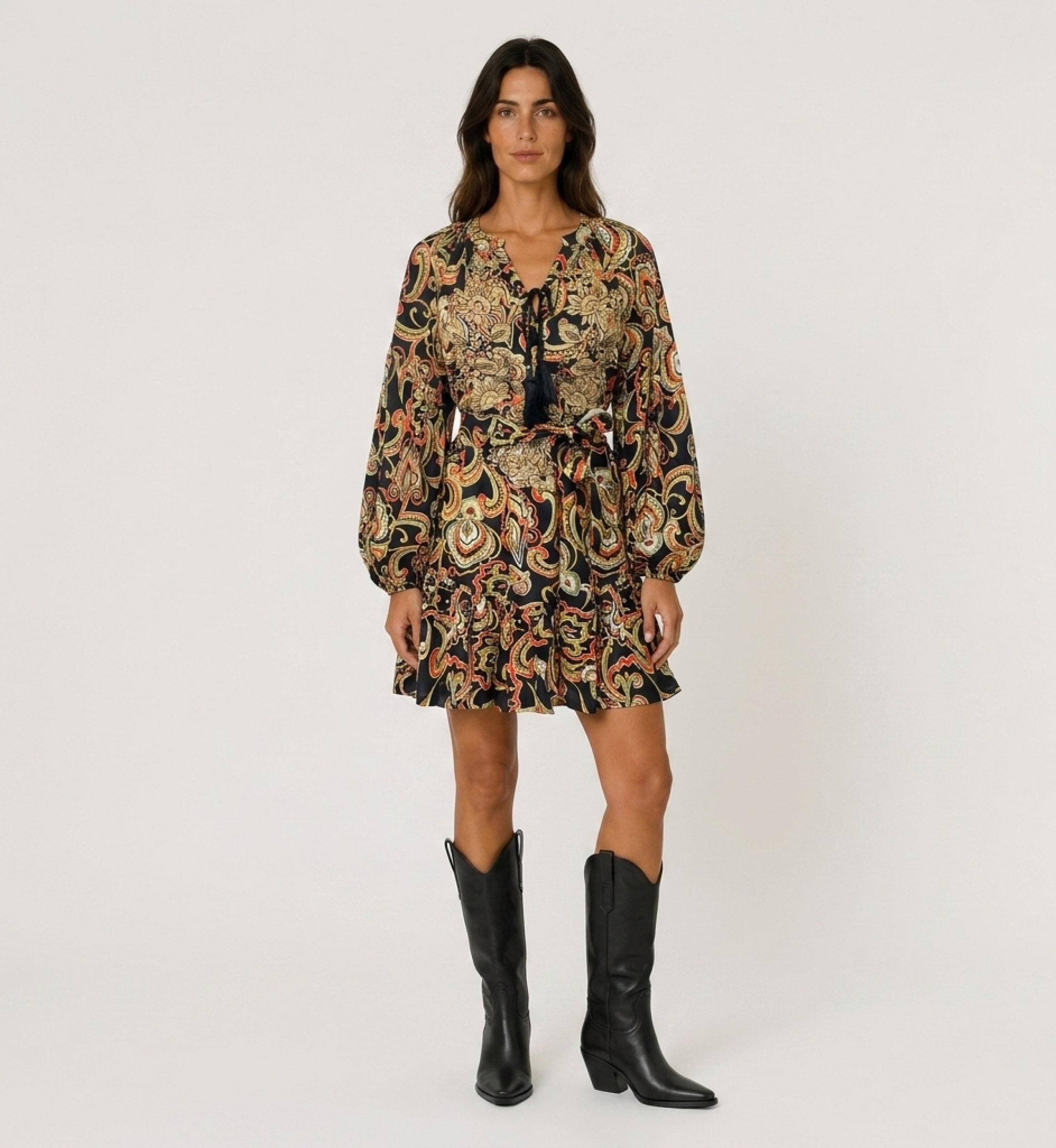 Black long-sleeve mini dress with colorful paisley print, tie neck with tassels, cinched waist, and ruffled hem, front view.