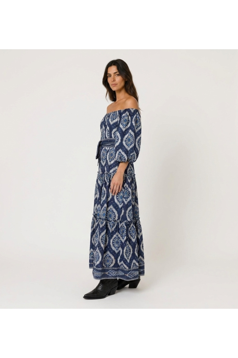 Vestido maxi azul marinho em camadas, ombros nus, padrões ikat brancos, mangas bufantes, cinto de amarrar.