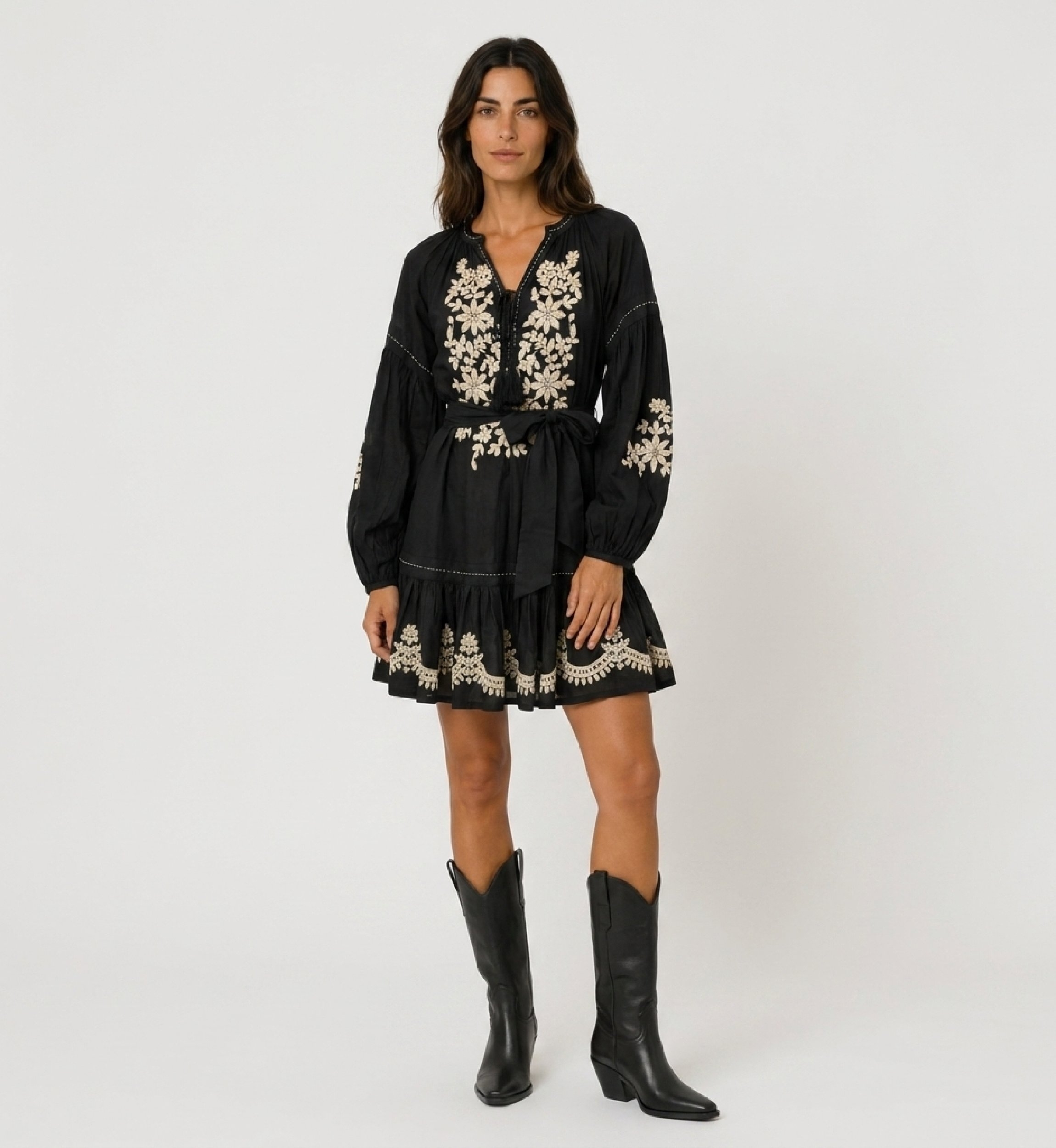 Minivestido negro holgado con mangas abullonadas, falda escalonada, bordado floral blanco y cintura con lazo, vista frontal.