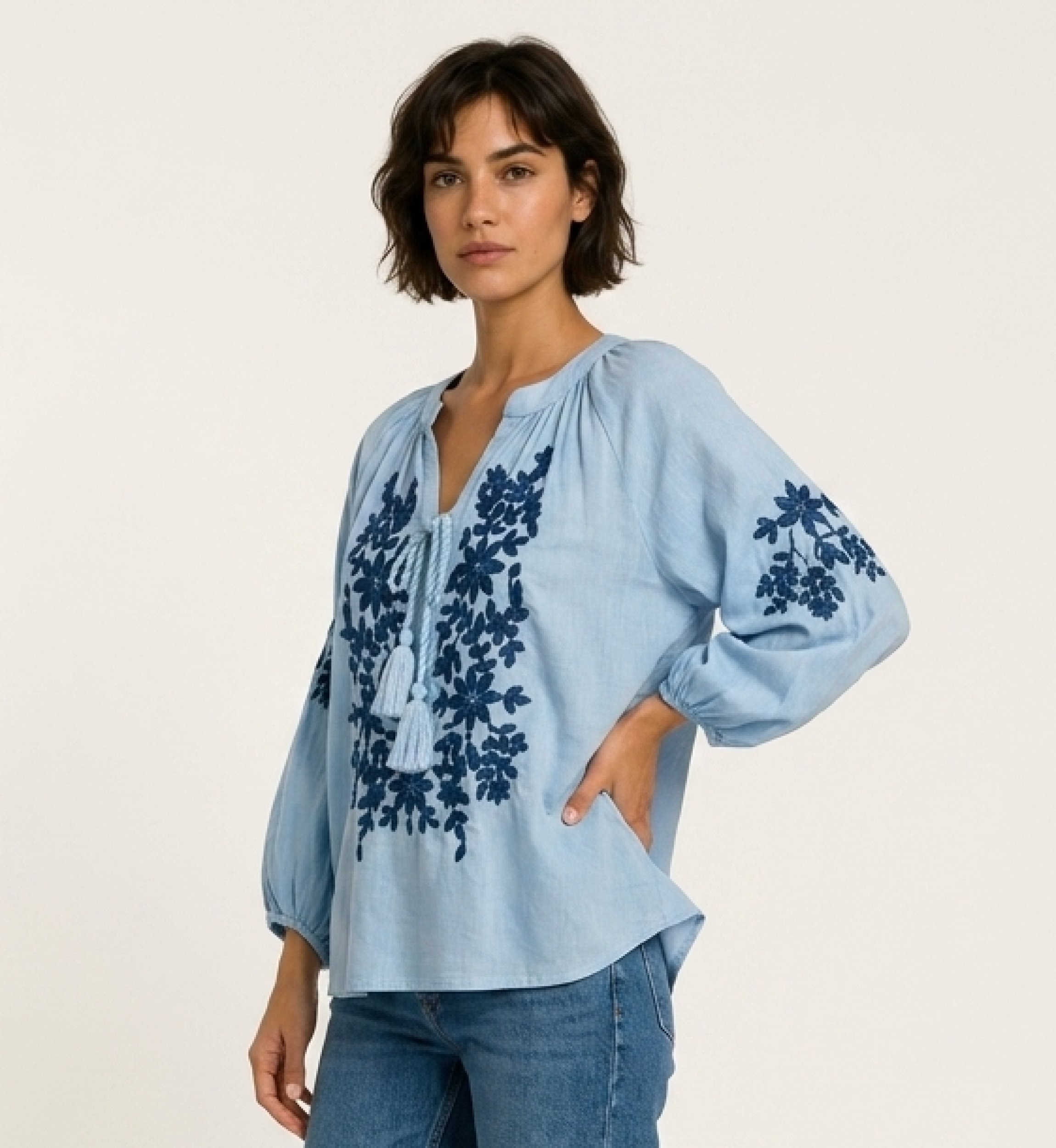 Blusa preta camponesa de manga longa, decote V com laço e bordado floral creme. Tecido tipo linho, vista 3/4.