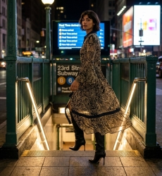 Vestido maxi longo preto e bege estampado, gola, botões, mangas sino, cintura com cordão, vista urbana noturna.