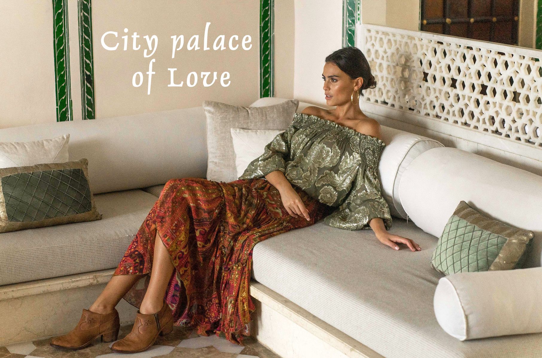Mannequin allongée sur une banquette blanche dans un intérieur élégant, portant un top kaki épaules dénudées et une jupe longue imprimée rouge, avec le texte « City palace of Love ».